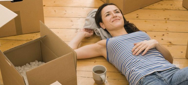 Woman surrounded by moving boxes, drinking coffee.